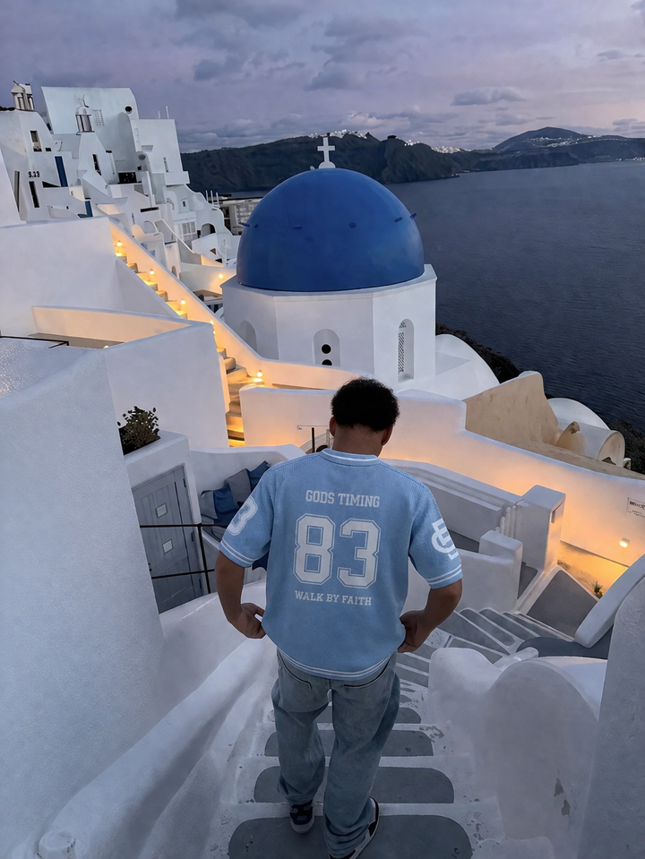 Benir Clothing light blue knit jersey with 83 graphic worn by a man on stairs in Santorini at sunset